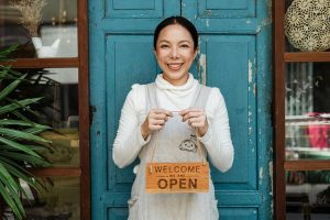Best Small Business Marketing Services in Hutchinson Island Florida a Woman Holding Up a Small Open Sign While Standing in Front of a Blue Door