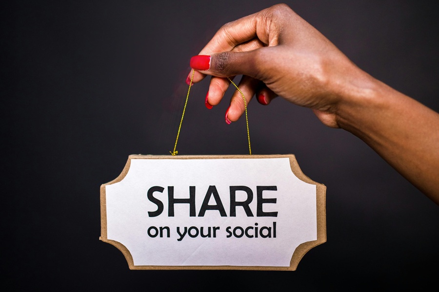 Best Small Business Marketing Company in Jupiter Farms Florida a Woman's Hand Holding Up a Small Hanging Sign That Says Share On Your Social