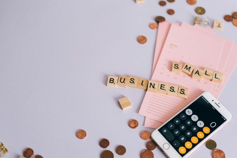 Best Google Business Profile Marketing Agency in Jupiter a Pink Folder with Letter Tiles on it Spelling Out Small Business with a Calculator App on a Phone and Pennies All Around