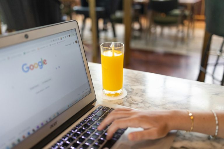 Google Business Profile Marketing Agency in Palm City Close Up of a Laptop on a Table with a Person's Hand on the Keyboard and a Glass of Orange Juice in the Background