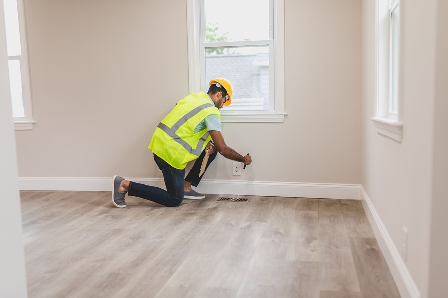 Home Services Marketing in Jupiter Florida a Man in a Yellow Reflective Vest Kneeling Down in a Room Holding a Tool to the Wall
